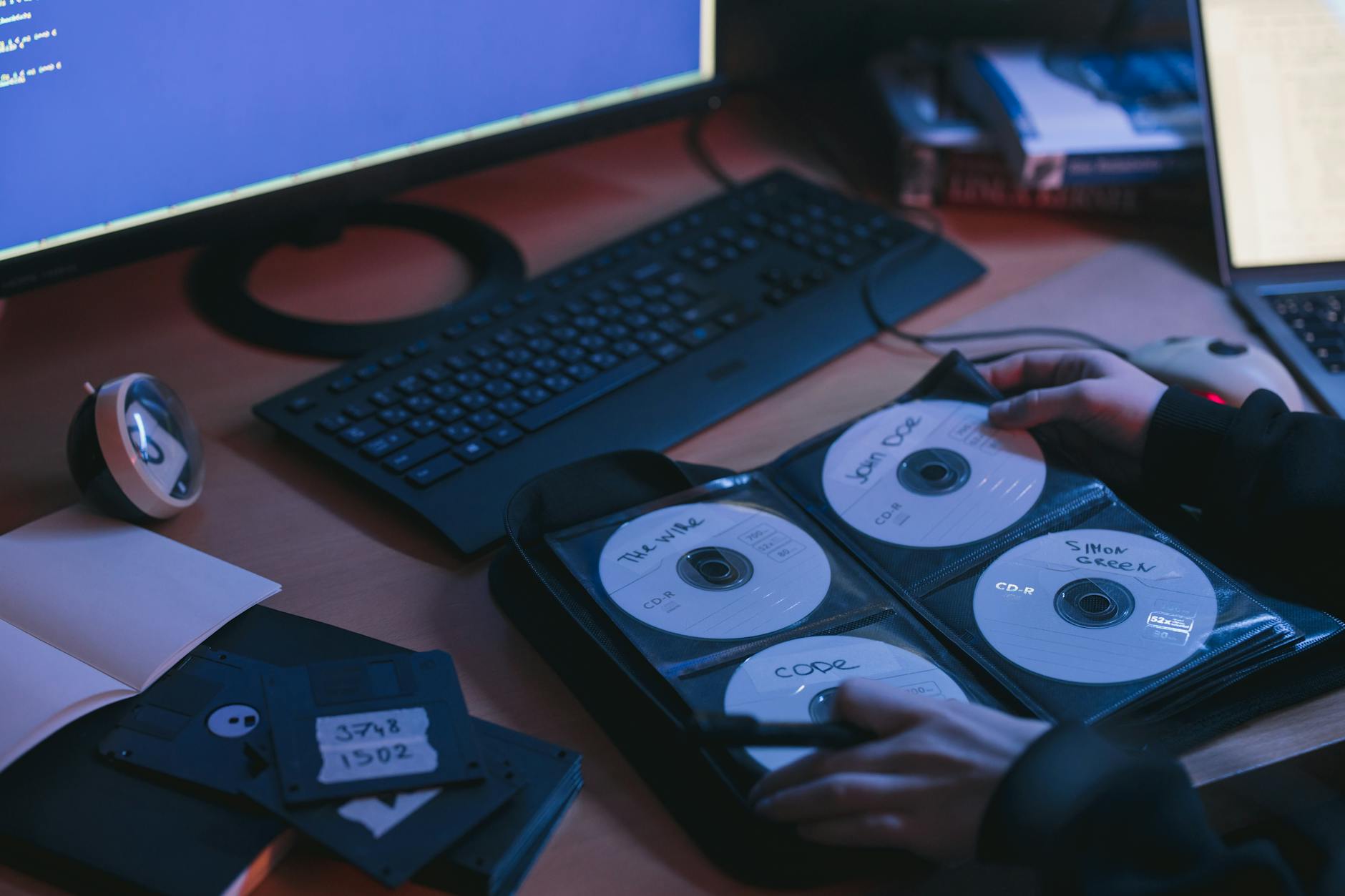 Dłonie przy biurku z płytami CD i dyskami w technologicznym otoczeniu Dłonie przy biurku z płytami CD i dyskami w technologicznym otoczeniu