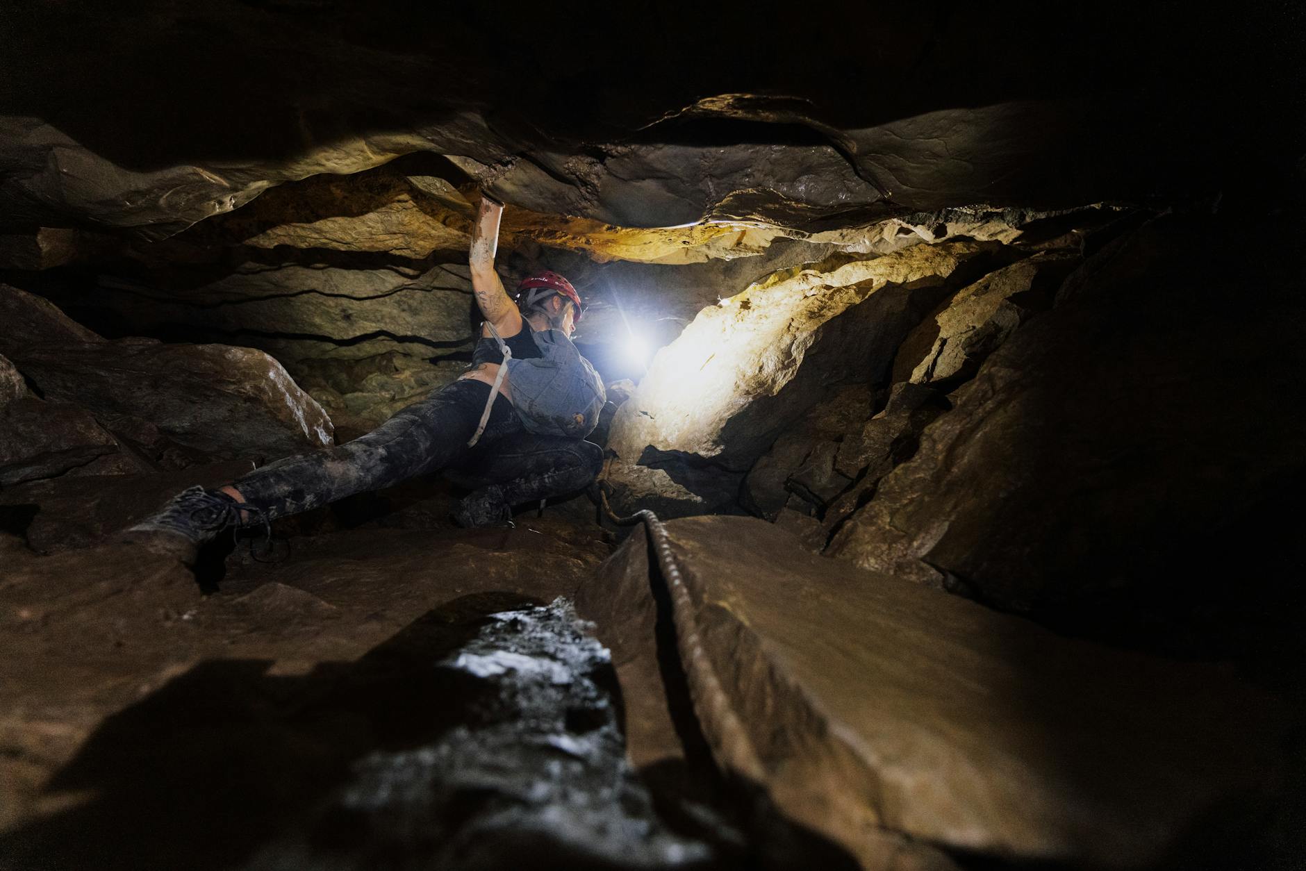 Speleolog początkujący przechodzi przez skalny korytarz z włączoną czołówką