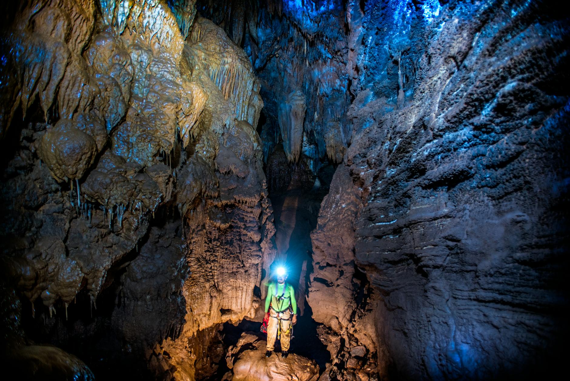 Speleolog z latarką eksploruje oświetloną jaskinię ze stalaktytami Speleolog z latarką eksploruje oświetloną jaskinię ze stalaktytami