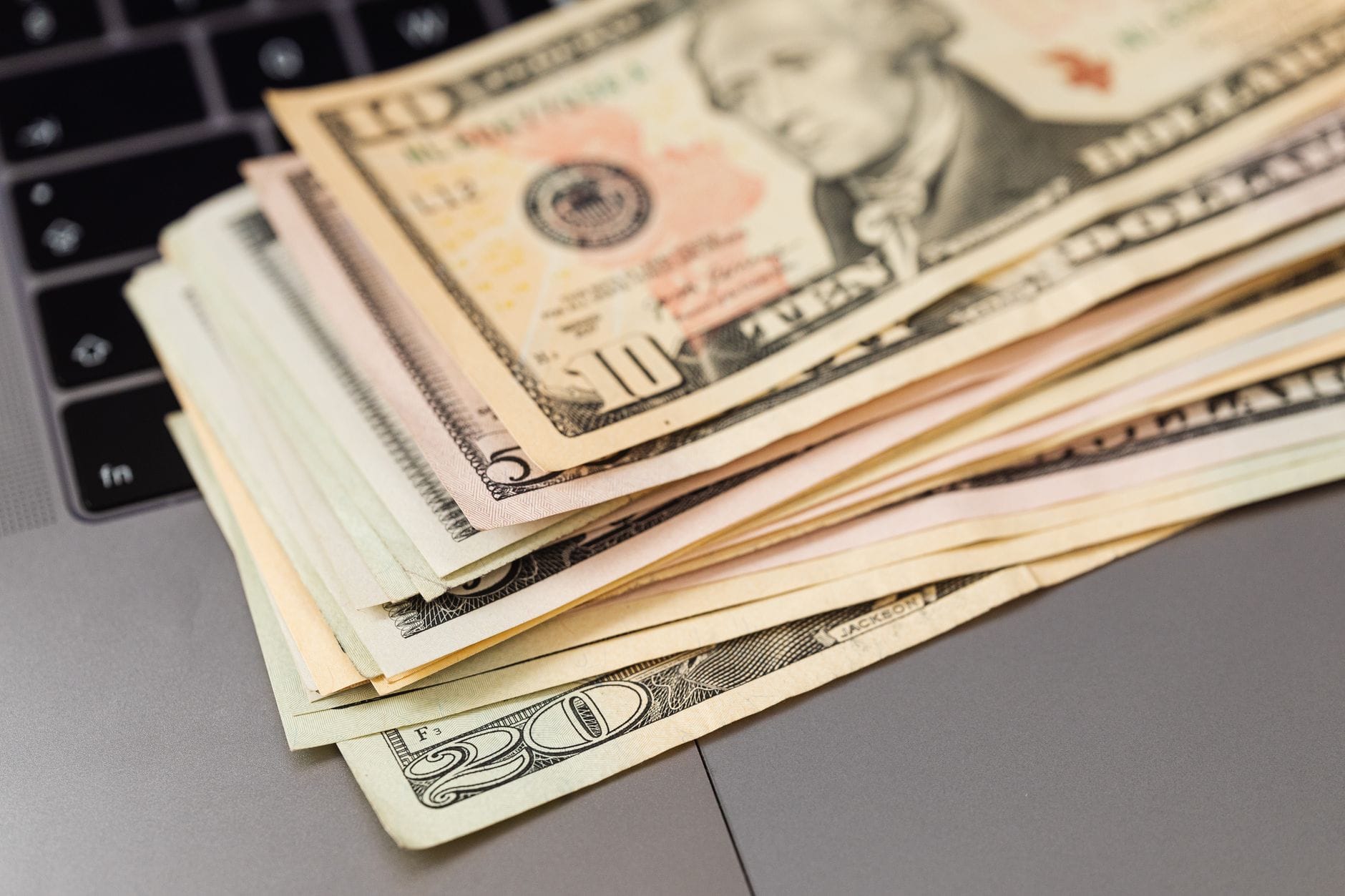 Plik banknotów dolarowych leżący na klawiaturze laptopa Plik banknotów dolarowych leżący na klawiaturze laptopa