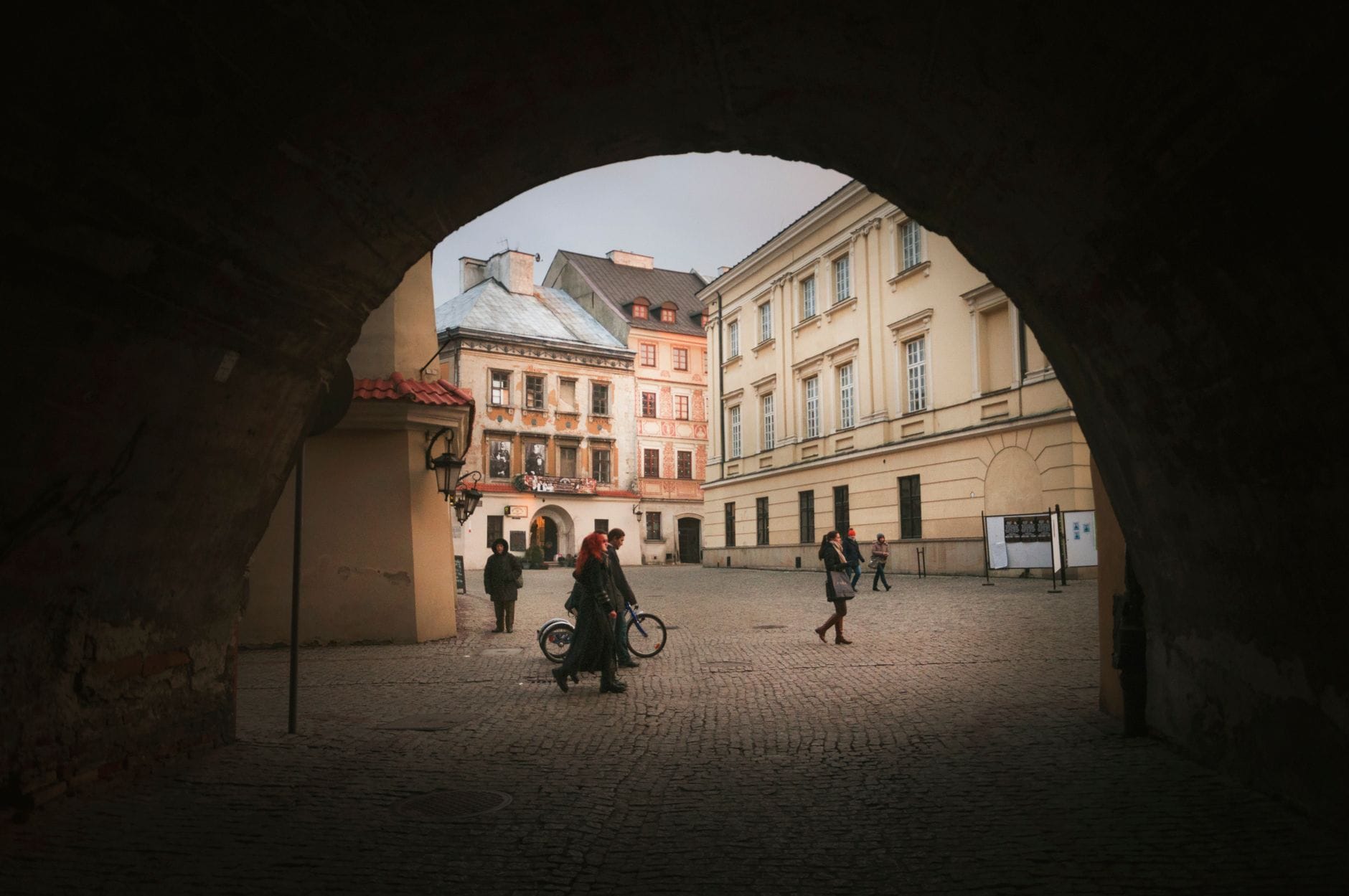 Przechodnie na brukowanej ulicy starego miasta widziani przez łuk