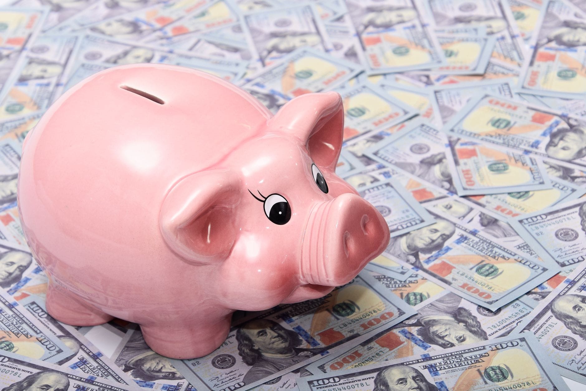 Różowa skarbonka stojąca na rozłożonych banknotach dolarowych