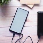 Jak rozpoznać dobrą przenośną ładowarkę po parametrach i certyfikatach Smartfon ładowany powerbankiem na drewnianym biurku
